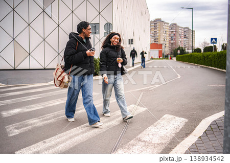 Two young adult women walking and smiling on urban street crossing Two young adult women walking and smiling on urban street crossing 138934542