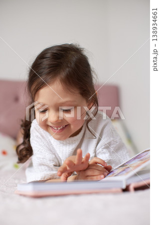 adorable child girl smiling while engaging with a storybook, fostering childhood development, literacy, and imagination at home 138934661