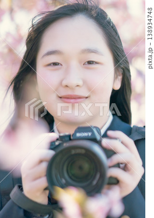 桜の下でカメラを構える女子高生 春の風景 カメラ部 趣味 学生 ポートレート 138934748