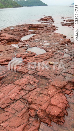 Layered deep red sedimentary rock formations with fractures and water pools in the seaside which is a remote coastal spots in Hung Shek Mun (Red Stone Gate), Plover Cove Country Park, Hong Kong Layered deep red sedimentary rock formations with fractures and water pools in the seaside which is a remote coastal spots in Hung Shek Mun (Red Stone Gate), Plover Cove Country Park, Hong Kong 138934787