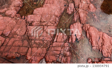 Layered deep red sedimentary rock formations with fractures and water pools in the seaside which is a remote coastal spots in Hung Shek Mun (Red Stone Gate), Plover Cove Country Park, Hong Kong 138934791