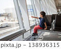 Young Boy Sitting in Airport Lounge Pointing Out of Window 138936315