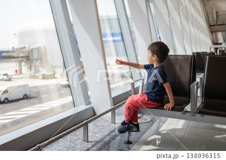 Young Boy Sitting in Airport Lounge Pointing Out of Window Young Boy Sitting in Airport Lounge Pointing Out of Window 138936315