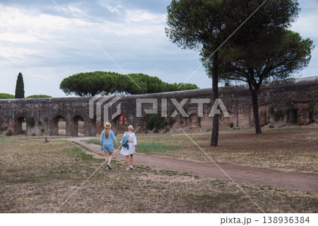Mother and teenage daughter holding hands walking near ancient Roman aqueduct in Parco degli Acquedotti Rome enjoying travel and cultural Italy 138936384