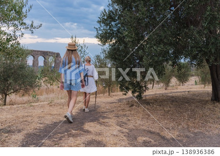 Walking mother and teenage daughter in Parco degli Acquedotti Rome near ancient Roman aqueduct ruins at sunset among trees and dry grass Walking mother and teenage daughter in Parco degli Acquedotti Rome near ancient Roman aqueduct ruins at sunset among trees and dry grass 138936386