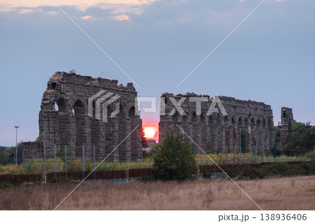 Ancient Roman aqueduct ruins at sunset in Parco degli Acquedotti Rome with dramatic sky and glowing sun between arches Ancient Roman aqueduct ruins at sunset in Parco degli Acquedotti Rome with dramatic sky and glowing sun between arches 138936406