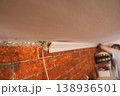 Installing white crown molding along ceiling near brick wall, home renovation process 138936501