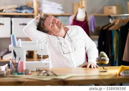 Sitting at workplace, man tailor does limbering-up, warms up numb muscles 138936598
