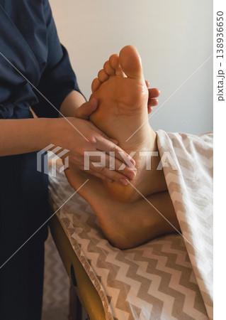 Therapist hands massaging person's foot, promoting relaxation well-being during spa treatment. Receiving relaxing massage during reflexology therapy 138936650