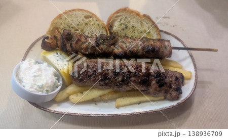 Pork skewer and lamb skewer served on the fries with tzatziki and bread on the side 138936709