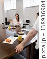 Woman delivering meeting notes at table with food and juice in office, seen from opposite side. Meeting, notes, food, juice, office, woman. 138936904