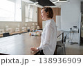 Businesswoman standing and speaking in bright open office area with desk near large windows. Speaking, office, desk, windows, businesswoman, modern. 138936909