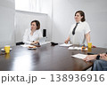 Smiling woman talking to colleague during breakfast business meeting at long table in modern office. Smiling, meeting, breakfast, woman, business. 138936916