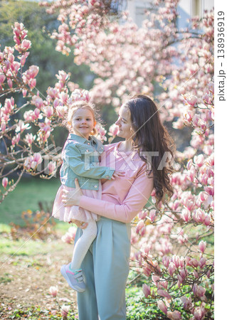 Young mother with her little daughter in a blooming magnolia garden in Prague. Symbol of maternal love and the beauty of springtime bonding in nature Young mother with her little daughter in a blooming magnolia garden in Prague. Symbol of maternal love and the beauty of springtime bonding in nature 138936919