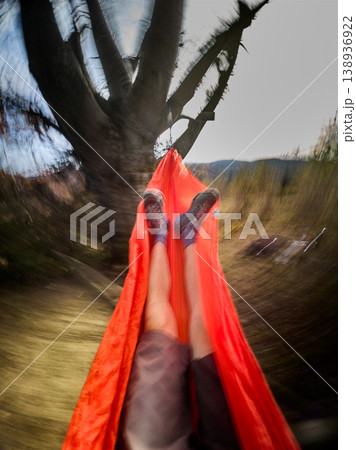 POV relaxing in hammock outdoors, motion blur effect showing swinging movement, legs view under tree in countryside with bright sky and nature landscape POV relaxing in hammock outdoors, motion blur effect showing swinging movement, legs view under tree in countryside with bright sky and nature landscape 138936922