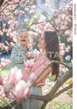 Trendy mom with her little daughter under blooming magnolia trees in a Prague park. Capturing a stylish family moment with a modern approach to parenting 138936946