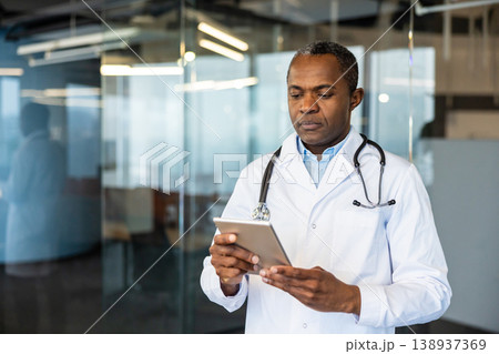 Experienced healthcare professional wearing a white coat and stethoscope using a digital tablet in a modern office environment, demonstrating medical technology and digital healthcare innovation 138937369