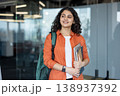 Young indian woman carrying a backpack, laptop, and notebooks, smiling and looking away while walking through a bright modern university campus building 138937392