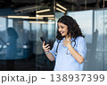 Female healthcare worker in scrubs and stethoscope joyfully reacting to good news on her mobile phone, reflecting achievement and happiness in a modern office environment 138937399