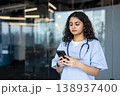 Young indian female doctor or nurse in light blue scrubs and stethoscope using a smartphone for telehealth, communication or medical app in a modern hospital or clinic setting 138937400