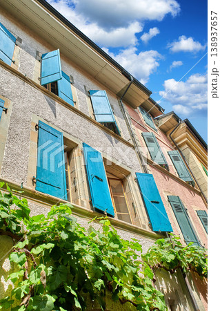 The classical architecture of a tall residential building with overgrown green plants on the wall. The exterior of an old apartment block on a sunny day. Bottom view of antique city flats The classical architecture of a tall residential building with overgrown green plants on the wall. The exterior of an old apartment block on a sunny day. Bottom view of antique city flats 138937657
