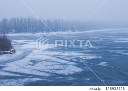 Winter landscape. Frozen river in fog on a cloudy day. Human footprints on ice in the middle of the river. Trees in the fog. Snow stripes. Dnipro. Kyiv, Ukraine Winter landscape. Frozen river in fog on a cloudy day. Human footprints on ice in the middle of the river. Trees in the fog. Snow stripes. Dnipro. Kyiv, Ukraine 138938328