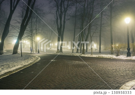 Alley of a night winter park in a fog. Footpath in a fabulous winter city park at night in fog with benches and latterns. Beautiful foggy evening in the Mariinsky Park. Kyiv, Ukraine. Alley of a night winter park in a fog. Footpath in a fabulous winter city park at night in fog with benches and latterns. Beautiful foggy evening in the Mariinsky Park. Kyiv, Ukraine. 138938333