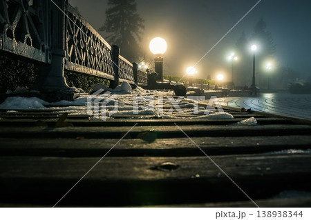 Wooden bench in the snow in a winter night park in the fog. Footpath in a winter city park at night in fog with benches and latterns. Beautiful foggy evening in the Mariinsky Park. Kiev, Ukraine. Wooden bench in the snow in a winter night park in the fog. Footpath in a winter city park at night in fog with benches and latterns. Beautiful foggy evening in the Mariinsky Park. Kiev, Ukraine. 138938344