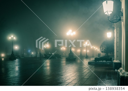 The main alley of a night winter park in a fog. Footpath in a fabulous winter city park at night in fog with benches and latterns. Beautiful foggy evening in the Mariinsky Park. Kyiv, Ukraine. The main alley of a night winter park in a fog. Footpath in a fabulous winter city park at night in fog with benches and latterns. Beautiful foggy evening in the Mariinsky Park. Kyiv, Ukraine. 138938354