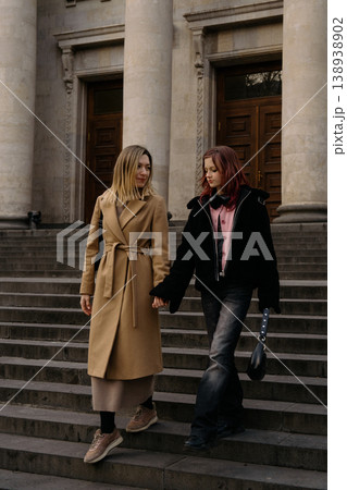 Mother and teenage daughter walk hand in hand down steps in a city setting on a sunny day 138938902