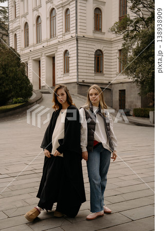 Two women stand on a city street near a building during a sunny day in the afternoon Two women stand on a city street near a building during a sunny day in the afternoon 138938909
