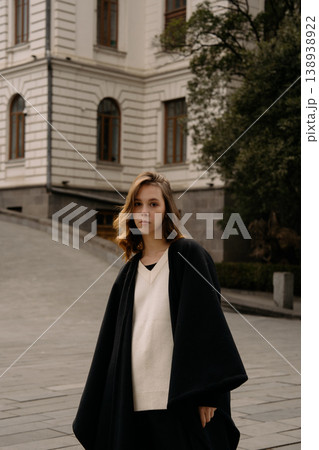 Girl in black coat stands on a city street near a historical building on a sunny day 138938922
