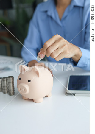 A person putting a coin into a piggy bank. Concept for saving and financial planning and wealth accumulation for retirement or future investment A person putting a coin into a piggy bank. Concept for saving and financial planning and wealth accumulation for retirement or future investment 138939833