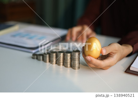 Rising stack of coins and golden eggs on the table. Businessman calculating dividend yield on the background for wealth management and investment concept. 138940521