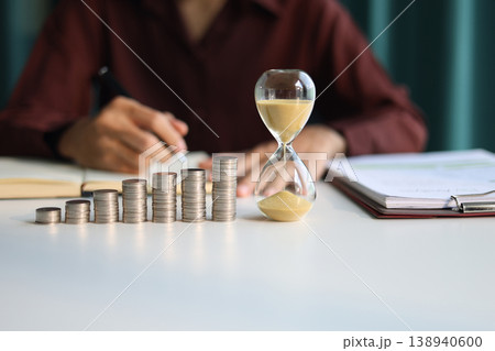 Rising stack of coins and running sand clock on the table. Growing of income, saving or return investment through time. Time and money concept. Rising stack of coins and running sand clock on the table. Growing of income, saving or return investment through time. Time and money concept. 138940600