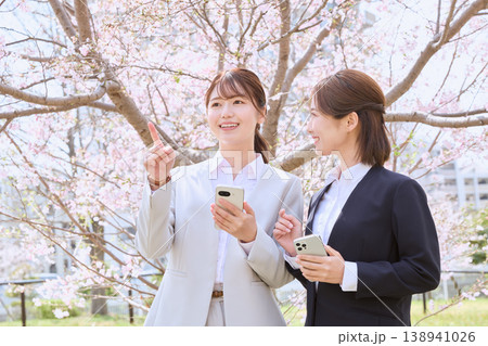 桜の下でスマートフォンを持ちながら会話する二人の若い女性ビジネスパーソン・新入社員の春のイメージ 138941026