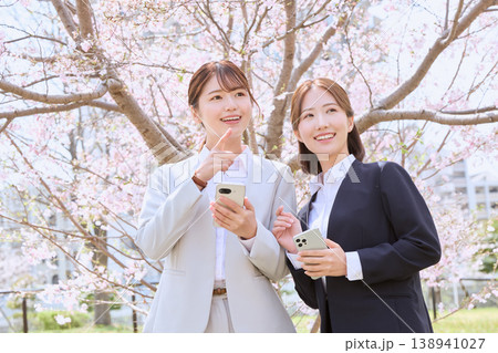 桜の下でスマートフォンを持ち笑顔で指差す二人の若い女性ビジネスパーソン・春の新入社員イメージ 桜の下でスマートフォンを持ち笑顔で指差す二人の若い女性ビジネスパーソン・春の新入社員イメージ 138941027