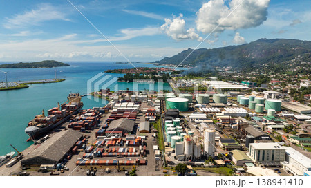 Large shipping containers and storage tanks located by the harbor, with green islands and turquoise waters in the background. Victoria. Seychelles, Mahe. Large shipping containers and storage tanks located by the harbor, with green islands and turquoise waters in the background. Victoria. Seychelles, Mahe. 138941410