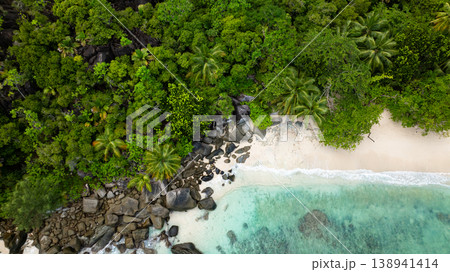 Lush green forest bordering a sandy beach with scattered rocks, leading into the turquoise water. Butzel Beach. Seychelles, Mahe. Lush green forest bordering a sandy beach with scattered rocks, leading into the turquoise water. Butzel Beach. Seychelles, Mahe. 138941414