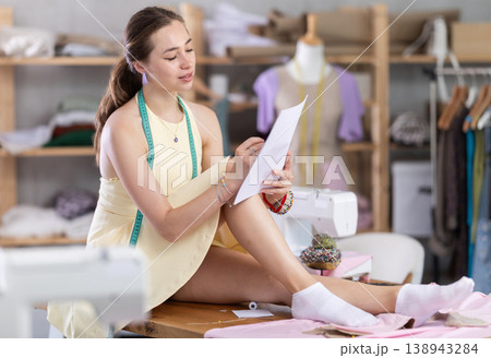 Girl sitting on table drawing sketches on white sheets Girl sitting on table drawing sketches on white sheets 138943284