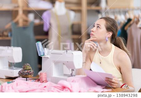 Upset young woman seamstress with documents in workshop Upset young woman seamstress with documents in workshop 138943298