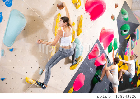 Young woman climbs steep artificial wall in sports complex and trains endurance 138943526