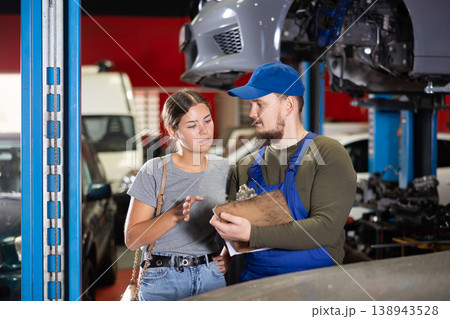 Male worker of auto service speaking to female client concerning his notes on paper Male worker of auto service speaking to female client concerning his notes on paper 138943528