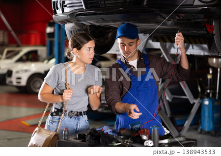 Guy mechanic checking woman client's car with measuring device Guy mechanic checking woman client's car with measuring device 138943533
