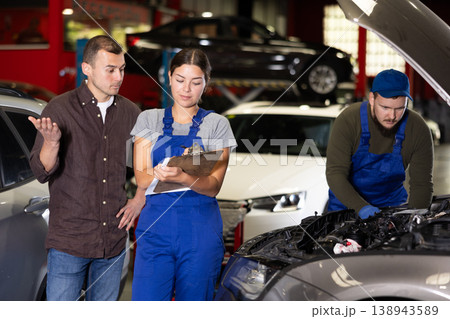 Female worker of auto service speaking to male client concerning her notes on paper Female worker of auto service speaking to male client concerning her notes on paper 138943589