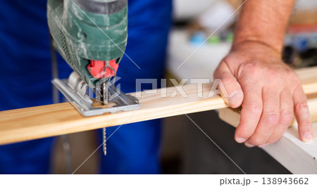 Cropped view of man using a jigsaw machine on wooden plank at home Cropped view of man using a jigsaw machine on wooden plank at home 138943662