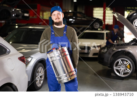Positive male worker of car workshop holding metal fuel canister Positive male worker of car workshop holding metal fuel canister 138943710