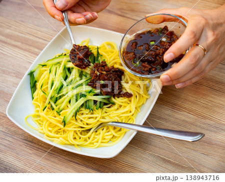 Hands pouring cucumber noodles with mushroom sauce. Chinese cuisine Hands pouring cucumber noodles with mushroom sauce. Chinese cuisine 138943716