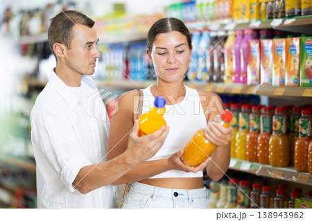 Positive couple choosing juice or soda while standing near glass display cases full of products in supermarket 138943962