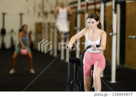 Portrait of young athletic girl training on an air-bike in gym Portrait of young athletic girl training on an air-bike in gym 138943977